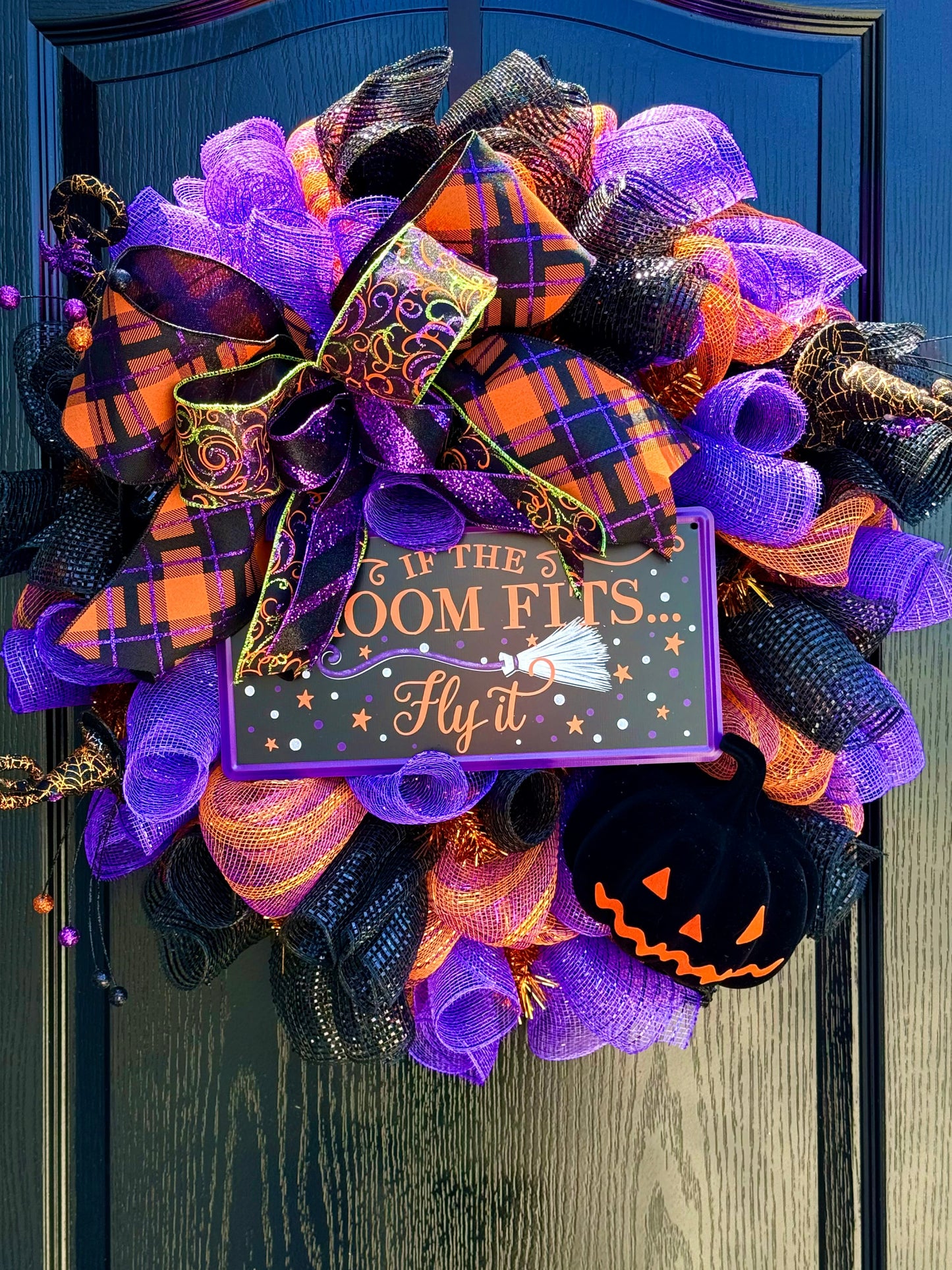 Halloween wreath with purple, orange, and black ribbons on a door.
